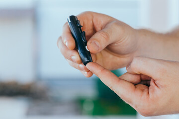 Fototapeta premium medicine, diabetes, medicine and people concept - close up of a man with a blood glucose meter and a test strip checking blood sugar at home. Diabetes Day, November 14