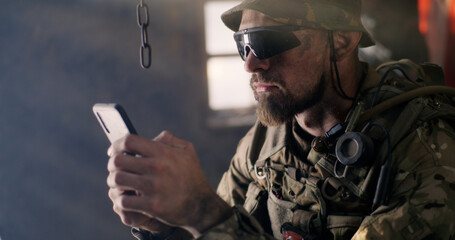 Military man using smartphone inside grungy building