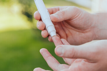 diabetes, glycemia, healthcare and people concept - close up of a man's hands using a lancet on his finger to check blood glucose meter