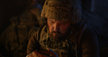 Fototapeta premium Depressed soldier drinking near fire at night
