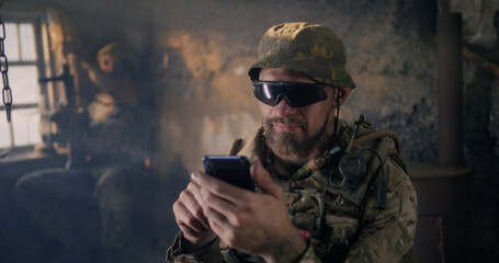 Military man using smartphone inside grungy building