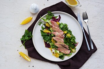 Warm salad with a mixture of salad leaves, baked duck and orange on a clay plate