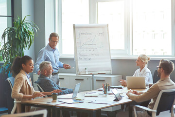 Start up team at brainstorming meeting. Confident mature businessman standing near flipchart in the...