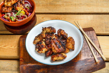 Plates of pan-Asian salad with sesame seeds and grilled chicken in pad thai sauce on wooden stands and loya chopsticks.