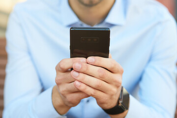 Businessman using smartphone while sitting on the bench outdoors, focus on mobile phone