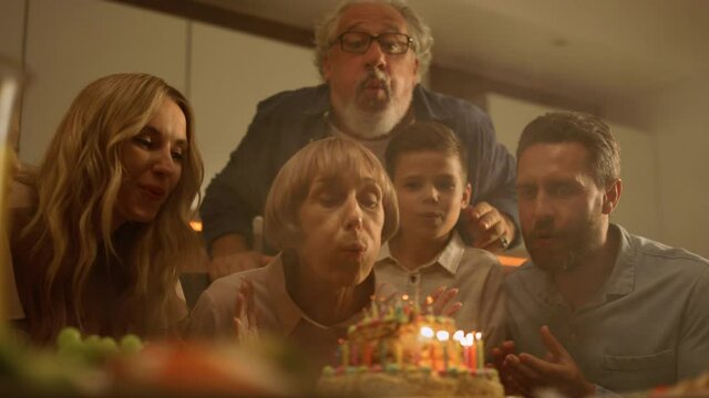 Family congratulating grandmother on birthday. Woman blowing candles on cake