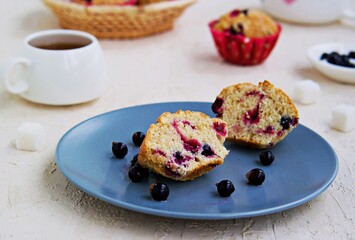 Muffins with black currants on a blue plate on a light concrete background. American cuisine.