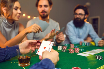 Man holding a chip and pair of aces while playing poker with his friends on casino night