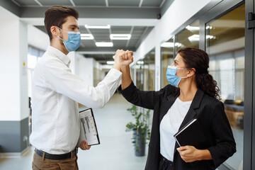 Young workers' special greeting during coronavirus to prevent coronavirus spread. Man and woman wearing medical masks crossed their hands to greet each other at the office. Health safety at work.