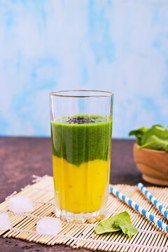 A healthy drink, a two-layer smoothie with fresh spinach and ripe mango in a tall glass glass on a dark concrete background.