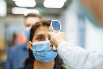 Office workers are checked with a distant non contact thermometer during coronavirus pandemic. Young business woman passing temperature control at the office corridor to prevent covid-19 spread.