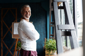 Smiling attractive Casual Grey-haired mature man standing near window looking at the camera