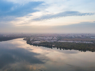 Aerial drone view. Lake on the outskirts of the city. The lake reflects the sky in the rays of the sunset. Cloudy.