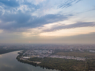 Aerial drone view. Lake on the outskirts of the city. The lake reflects the sky in the rays of the sunset. Cloudy.