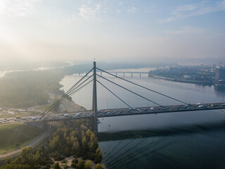 Fototapeta premium Aerial drone view. North bridge in Kiev in the rays of a sunny morning. Autumn haze in the air, cars are driving across the bridge.