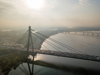 Fototapeta premium Aerial drone view. North bridge in Kiev in the rays of a sunny morning. Autumn haze in the air, cars are driving across the bridge.