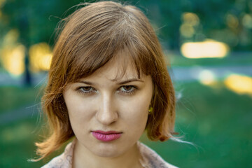 Angry face of a young white woman in a public park on a summer evening.