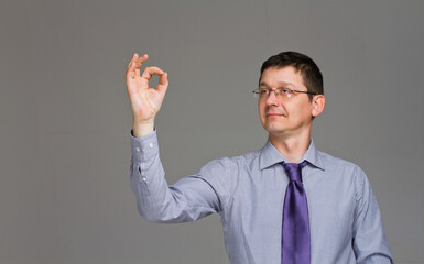 Copy space at his hand. Happy mature man in shirt and tie pointing copy space and smiling while standing against grey background