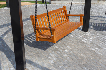 New swing bench in the park. Swing in the form of a wooden park bench. Swing in the recreation area.