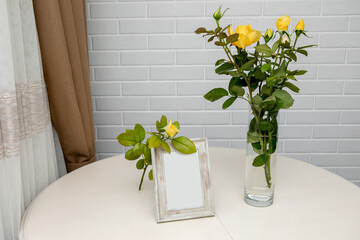 Blank photo frame and yellow roses in the vase standing over the white wall