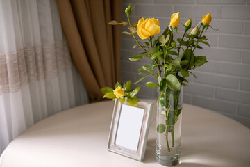 Blank photo frame and yellow roses in the vase standing over the white wall