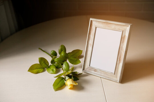 Blank photo frame and yellow roses over the white wall