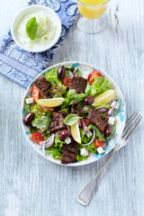 Tasty Salad with Grilled Beef Pieces, Cherry Tomatoes, feta Cheese and Kalamata Olives. Bright wooden background. Top view.	