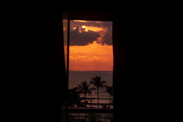 beautiful orange sunrise on the beach with coconut trees from the perspective of a window (nascer do sol pela janela)