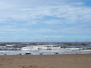 the beach at blundell flats in southport with waves braking on the beach and the wind turbines at burbo bank visible in the distance