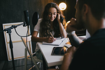 Young woman blogger interviewing man in a studio, using microphone and laptop.