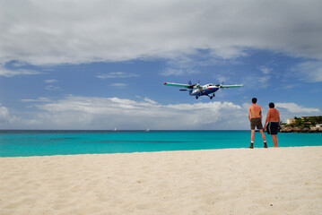 Obraz na płótnie Canvas Two male beachgoers watch a plane land in St Maarten