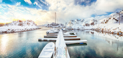 Charming winter scenery with yachts and boats nier pier in small fishing village and snowy ...