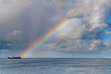 Rainbow over the Caribbean Sea ending at a freighter