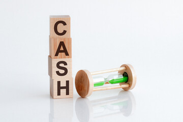 Close-up of an hourglass next to wooden blocks with the text CASH