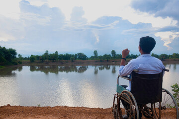 Young disabled man with river background.He is sitting on wheelchair and looking into river.despair,lonely,hope.Photo concept depression and Patient.