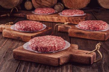 Raw hamburgers on cutting board with wood pile background