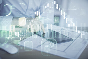 Double exposure of man's hands holding and using a digital device and forex graph drawing. Financial market concept.