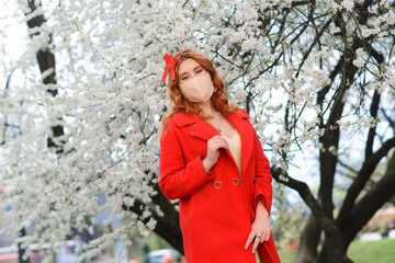 Young woman in a protective sterile medical mask on her face in the spring garden.