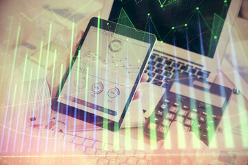 Double exposure of man's hands holding and using a digital device and forex graph drawing. Financial market concept.