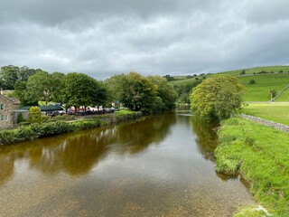 View looking down the River Wharfe, with old trees, cars fields, and distant hills in, Burnsall, Skipton, UK