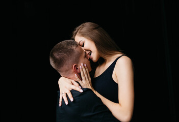 Man and woman kissing each other on a black background. The girl bites the guy on the nose. Black background Guy and girl holding hands. Couple hugging. Love.