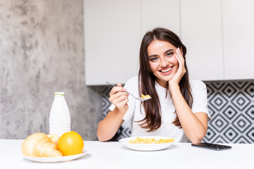 Smiling young woman eating breakfast cereals of bowl at home.