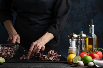 Close-up view of professional chef cuts octopuses for cooking, on the background of vegetables on a dark blue background. Asian cuisine. Traditional recipe. Seafood concept. Backstage of preparing