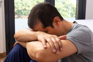 Side view of a sad man sitting on a floor in the bedroom at home
