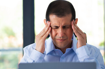 Sick executive with migraine complaining in pain rubbing temples sitting on a desk at office