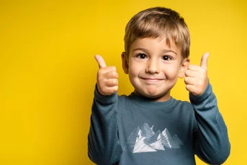Fotobehang Portrait of happy small caucasian boy in front of yellow background thumbs up - Childhood growing up and achievement concept - front view waist up copy space © Miljan Živković