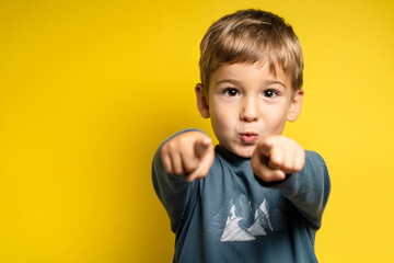 Portrait of happy small caucasian boy in front of yellow background pointing finger - Childhood growing up and achievement concept - front view waist up copy space