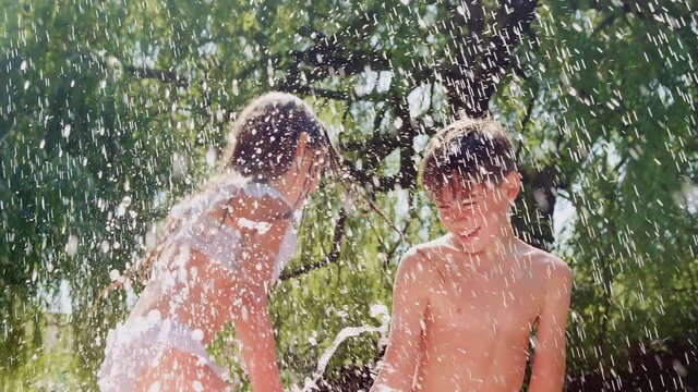Boy and girl in swimming costumes splashing in paddling pool in summer back yard - shot in slow motion