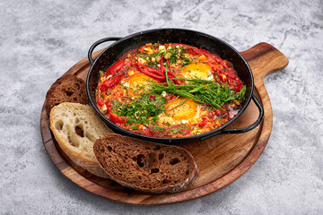 shakshuka on a frying pan and a wooden board, with green onions, bell peppers and croutons, on a white background