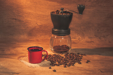 Red coffee mug with coffee grinder in the background. Rustic wooden background